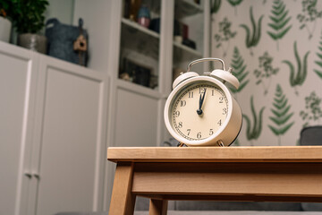Naklejka premium Alarm clock stands on a wooden table in living room with a modern interior with green plants