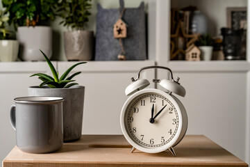 Alarm clock stands on a wooden table in living room with a modern interior with green plants