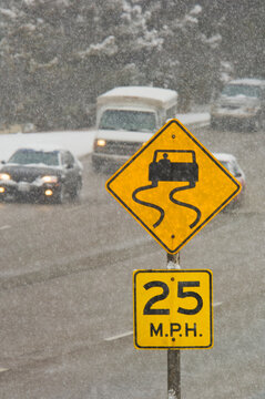 Traffic driving on snowy road with road sign warning of skid danger.