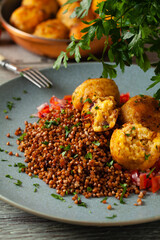 Lentil and millet meatballs. Served on tomato salsa with buckwheat. Gray plate, wooden boards in the background. Front view.