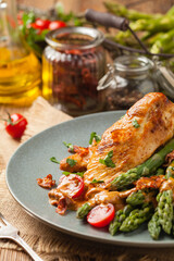 Roasted chicken breast, served on asparagus with tomato sauce, dried tomatoes. Front view.