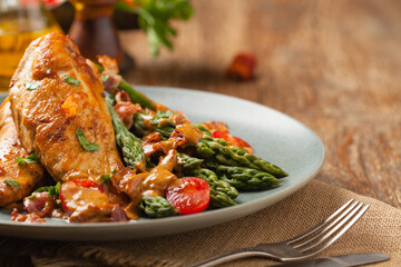 Roasted chicken breast, served on asparagus with tomato sauce, dried tomatoes. Front view.