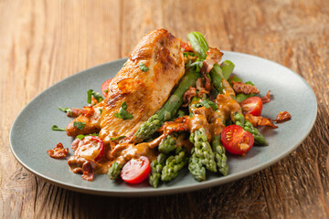 Roasted chicken breast, served on asparagus with tomato sauce, dried tomatoes. Front view.