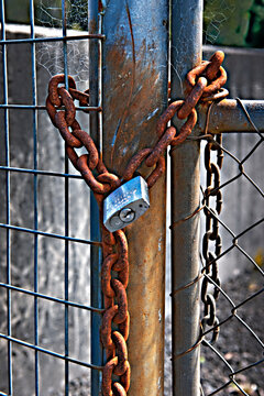 Rusty chain and padlock on a metal fence gate.