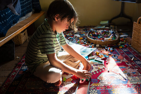 Boy sitting among toys on his bedroom floor in a patch of sunlight