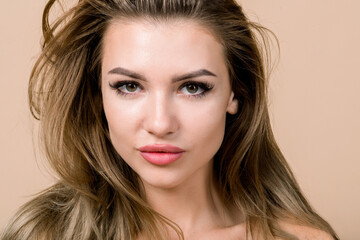 Fototapeta premium Close up beauty portrait of attractive young stunning European blond woman with natural make up, looking at camera, over beige background with copyspace. Beauty, skin care, cosmetology