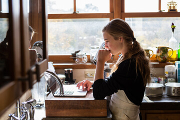 Teenage girl in a kitchen following a baking recipe on a laptop. 