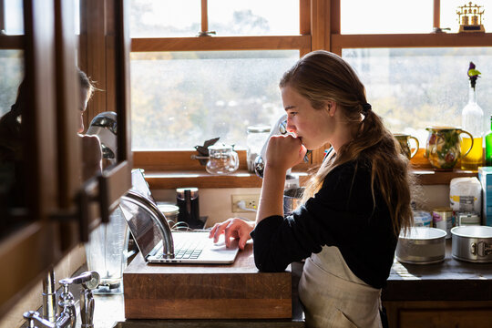 Teenage girl in a kitchen following a baking recipe on a laptop. 