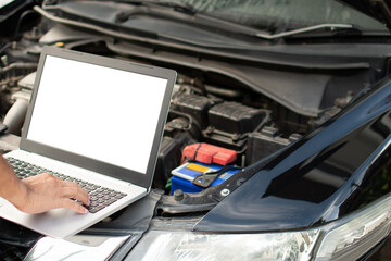 Closeup, A man's hand typing on a laptop computer keyboard to check the operation of the car engine in the garage. The engine of a car does not start. A notebook computer is a white screen and a blank