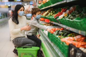 Mom and son wearing protective masks choose fruits to buy in the store