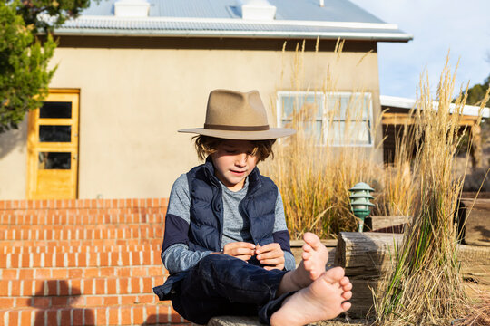 Portrait of young boy wearing fedora hat relaxing on his porch