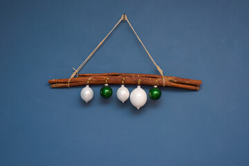 White and green christmas ornament balls hanging on hooks on big cinnamon stick on cord against blue painted wall