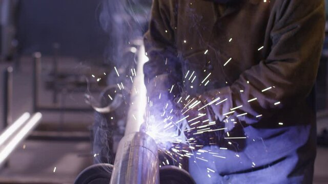 Worker welding metal pipe in big factory