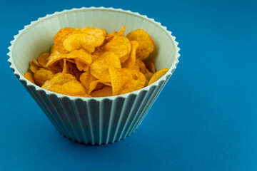 A bowl of potato chips on a blue background with copy space. Party snack.