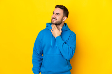 Young caucasian handsome man isolated on yellow background looking up while smiling