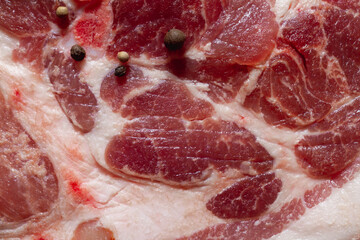 A piece of fresh pork neck meat with layers of fat and bone with spices, pepper peas close-up.