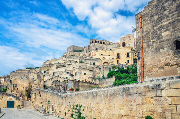 Fototapeta na wymiar Stone streets and buildings in Matera town historical centre Sasso Caveoso of old ancient town Sassi di Matera, blue sky white clouds, UNESCO World Heritage Site, Basilicata, Southern Italy