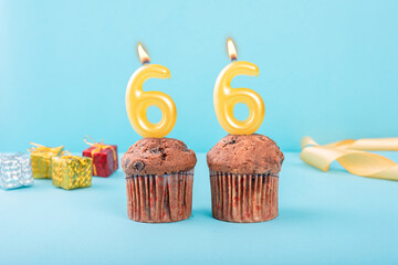 66 Number gold candle on a cupcake against a pastel blue background sixty six year celebration