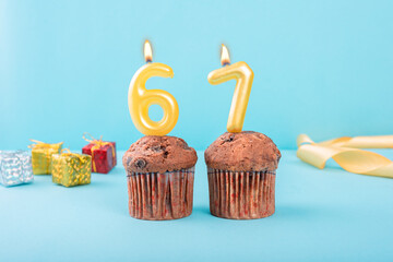 67 Number gold candle on a cupcake against a pastel blue background sixty seven year celebration