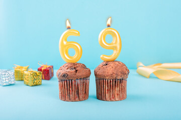 69 Number gold candle on a cupcake against a pastel blue background sixty nine year celebration