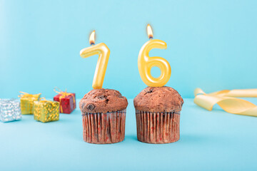 76 Number gold candle on a cupcake against a pastel blue background seventy six year celebration