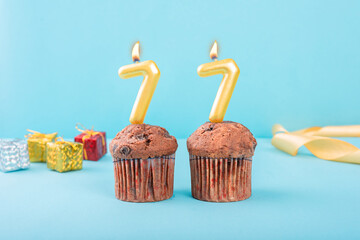 77 Number gold candle on a cupcake against a pastel blue background seventy seven year celebration