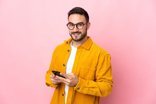 Young caucasian handsome man isolated on pink background sending a message with the mobile