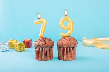 79 Number gold candle on a cupcake against a pastel blue background seventy nine year celebration