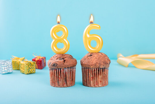 86 Number gold candle on a cupcake against a pastel blue background eighty six year celebration