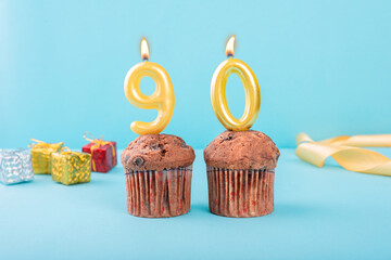 90 Number gold candle on a cupcake against a pastel blue background ninety year celebration