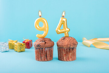 94 Number gold candle on a cupcake against a pastel blue background ninety four year celebration