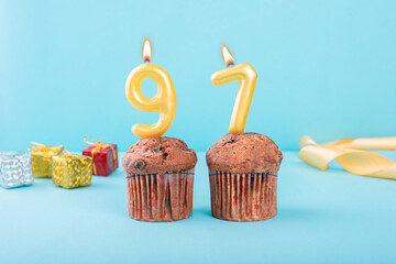 97 Number gold candle on a cupcake against a pastel blue background ninety seven year celebration