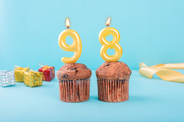 98 Number gold candle on a cupcake against a pastel blue background ninety eight year celebration