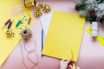 DIY concept.How to make Christmas card.New Year idea for children. Step-by-step photo instructions. card with christmas tree.Children's creativity.Step 2.Kid holds scissors and cuts a tree from paper.