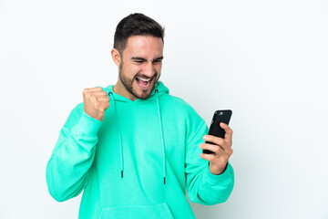 Young caucasian handsome man isolated on white background using mobile phone and doing victory gesture