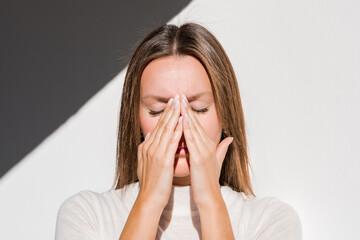 Woman feeling unwell, painful headache because of sinus ache, sinusitis, sinus pressure. Sad woman holding her nose and head because sinus pain. Coronavirus symptoms