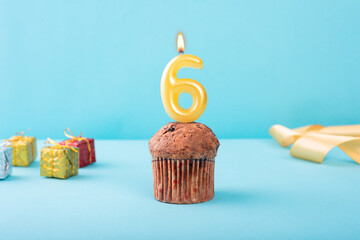 6 Number gold candle on a cupcake against a pastel blue background six year celebration 