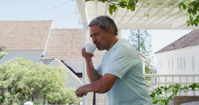Senior mixed race man drinking coffee on balcony in garden