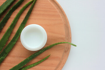Aloe vera cream and plant on wooden background. Flat lay composition with homemade cream in glass jar and ingredient. Copy space. 