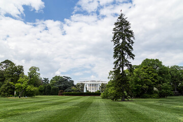 Fototapeta premium Wide shot of the White House South Lawn in Washington D.C., featuring the iconic neoclassical architecture and lush green grounds under a bright, cloudy sky in spring