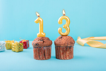 13 Number gold candle on a cupcake against a pastel blue background thirteen year celebration