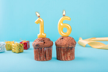 16 Number gold candle on a cupcake against a pastel blue background sixteen year celebration
