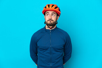 Young cyclist man isolated on blue background and looking up