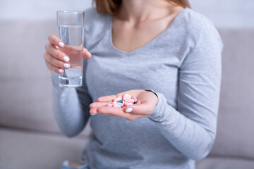 Desperate young woman holding handful of pills and glass of water, ready to commit suicide, closeup