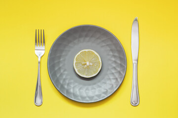 Plate with slice of lemon on yellow background. Diet concept. Colors of the year are Ultimate Gray and Illuminating.