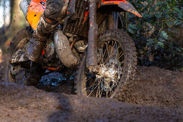 Muddy lower part of enduro motorcycle and its rider riding off road