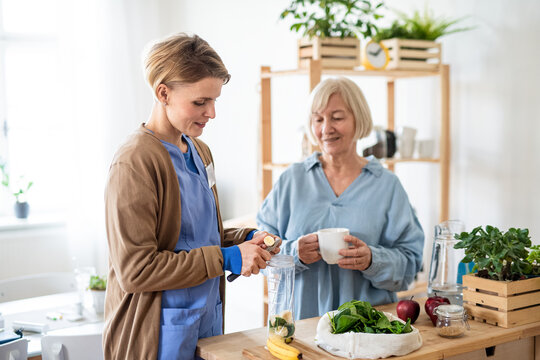 Senior woman with caregiver or healthcare worker indoors, preparing food.