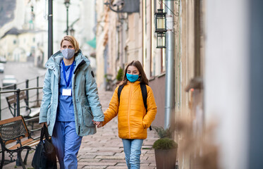 Woman healthcare worker outdoors on the way to work with schoolgirl daughter, coronavirus concept.