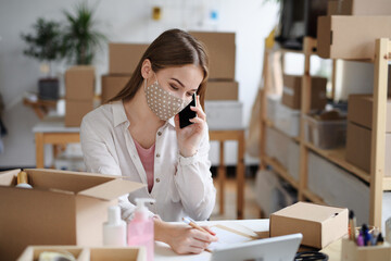 Young woman dropshipper with smartphone working at home, coronavirus concept.