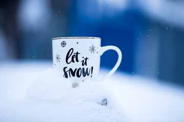 White Christmas cup on a snowdrift, blue background, outside. Mug with the inscription: "Let it snow"! Chrismas time, wintertime.